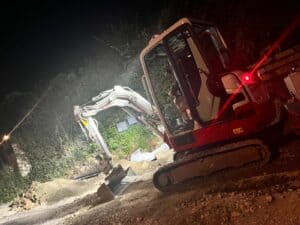 Ein roter Bagger bei Nacht arbeitet auf einer Baustelle, stark beleuchtet.