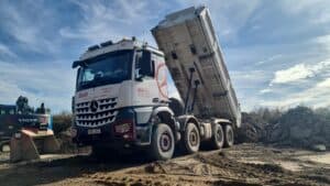 Ein Lastwagen mit angehobenem Kipper auf einer Baustelle, blau-weißer Himmel im Hintergrund.